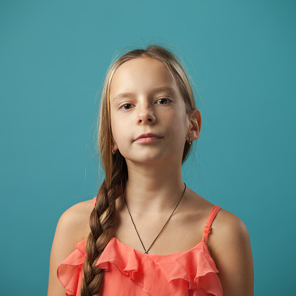 Studio close-up portrait of a 10 year old blonde girl in a pink sundress on a blue background