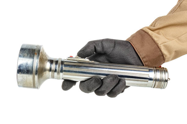 istock Large old aluminum flashlight in worker hand in black protective glove and brown uniform isolated on white background 1226670940