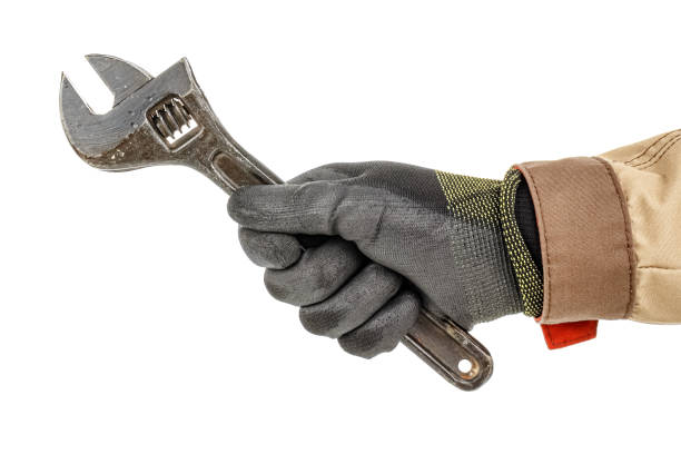 istock Worker hand in black protective glove and brown uniform holds large old adjustable wrench isolated on white background 1226670974