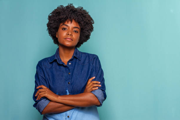 Black young woman with black power hair wearing a blue jeans shirt on blue background Black woman with curly hair wearing a blue jeans shirt on blue background brazilian culture stock pictures, royalty-free photos & images