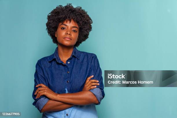 Black Young Woman With Black Power Hair Wearing A Blue Jeans Shirt On Blue Background Stock Photo - Download Image Now