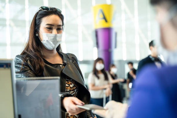 Asian female traveler giving passport to customer check in officer at airline service counter. Woman wearing face mask when traveling by airplane transportation to prevent covid19 virus pandemic. Asian female traveler giving passport to customer check in officer at airline service counter. Woman wearing face mask when traveling by airplane transportation to prevent covid19 virus pandemic. passing giving photos stock pictures, royalty-free photos & images