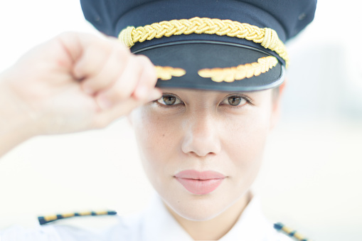 Close up portrait of a pretty female pilot wearing a captain uniform, saluting proudly at the airport. Aviation industry.