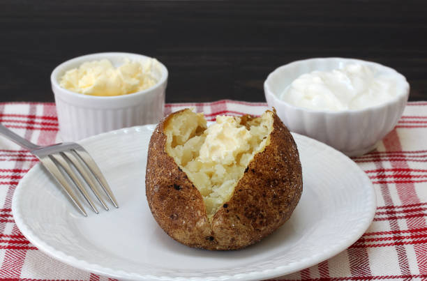 Baked potato, salted, with a dab of butter. One fresh baked russet potato with a dab of butter.  Close up, macro view. baked potato sour cream stock pictures, royalty-free photos & images