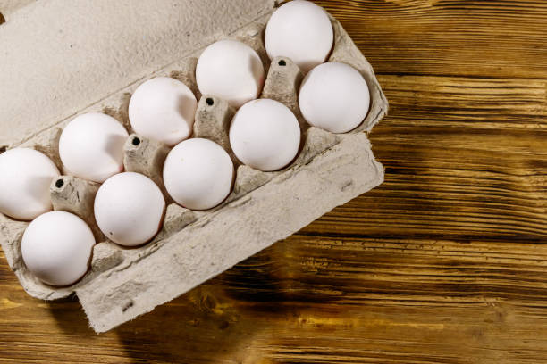 istock Raw chicken eggs in cardboard egg box on wooden table. Top view 1226697209