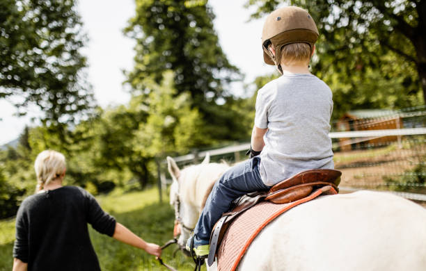 giovane donna che insegna a un ragazzo come cavalcare un cavallo - teaching child horseback riding horse foto e immagini stock