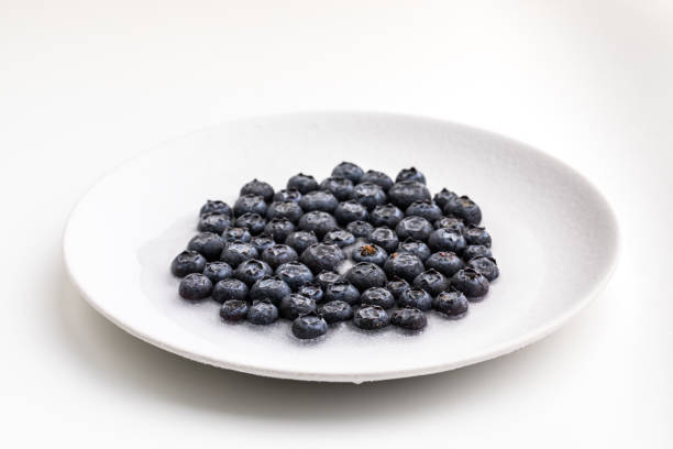 Frozen blueberries in white plate on white background.