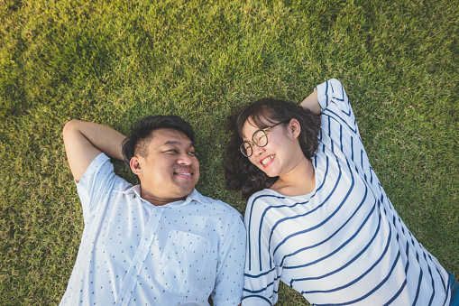 Happy young Asian couple holding hands and laying down on grass in the park, Couple relaxing and spending time together at outdoors, People and lifestyle concept