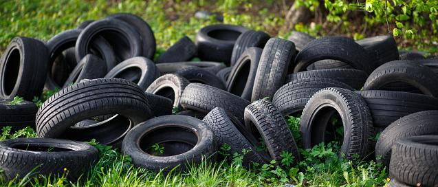 Dump of old used tires on fresh green grass in the forest. The problem of ecology and environmental pollution, processing of rubber waste from production and the automotive industry