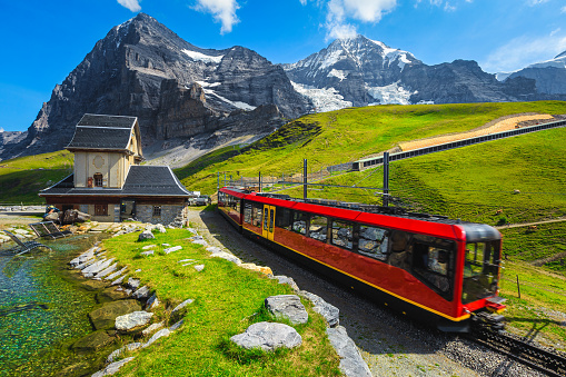 Modern red passenger train near the small mountain chapel. Cogwheel red tourist train coming down from the mountain station, Jungfraujoch, Bernese Oberland, Switzerland, Europe