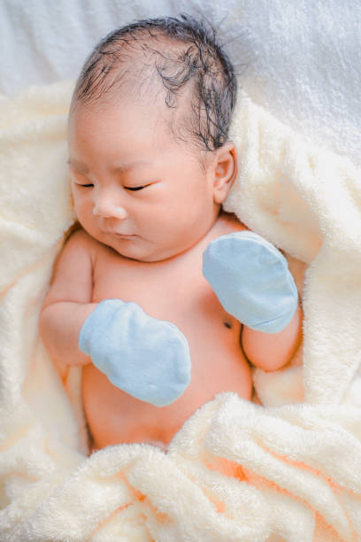 The Asian newborn baby boy wears the blue glove after shower on a yellow towel. stock photo