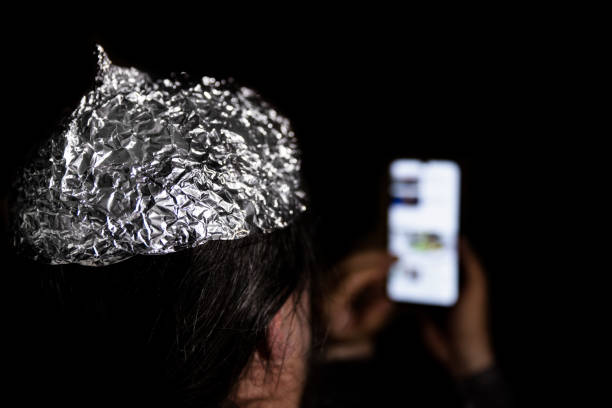 man in the dark wearing a tin foil hat, smartphone in the hand, conspiracy theory and mind control - tin foil hat imagens e fotografias de stock