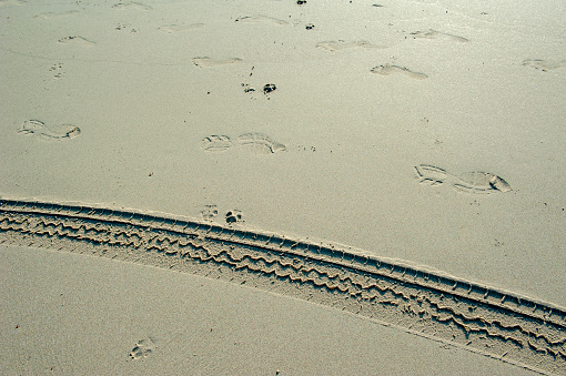Landscape view of tire tracks on the sandy beach leading into the horizontal sea with orange sunlight ray effect on horizon view background.