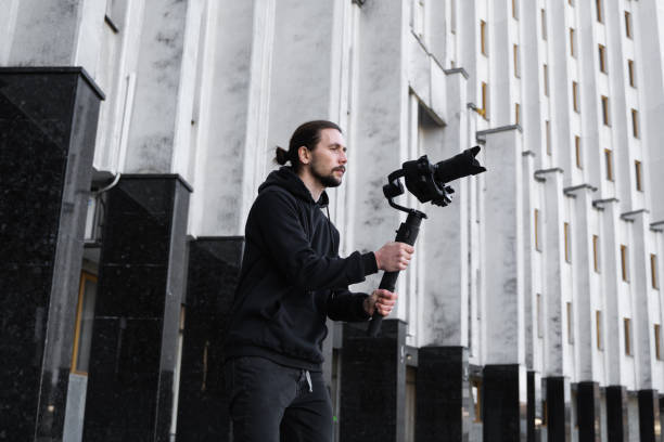 istock Young Professional videographer holding professional camera on 3-axis gimbal stabilizer. Pro equipment helps to make high quality video without shaking. Cameraman wearing black hoodie making a videos. 1226718428