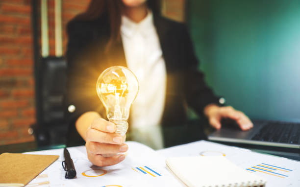 istock a businesswoman holding a glowing light bulb while working on laptop computer in office 1226718533