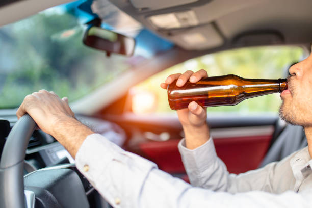 Drunk asian young man drives a car with a bottle of beer with sunset background Drunk asian young man drives a car with a bottle of beer with sunset background, Dangerous driving concept arrest photos stock pictures, royalty-free photos & images
