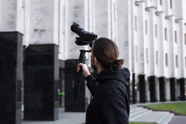 istock Young Professional videographer holding professional camera on 3-axis gimbal stabilizer. Pro equipment helps to make high quality video without shaking. Cameraman wearing black hoodie making a videos. 1226721309