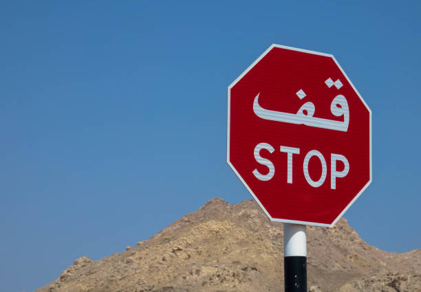 znak stop, w języku arabskim i angielskim skrypt na tle pasma górskiego i bezchmurnego nieba - sign stop sign arabic script oman zdjęcia i obrazy z banku zdjęć