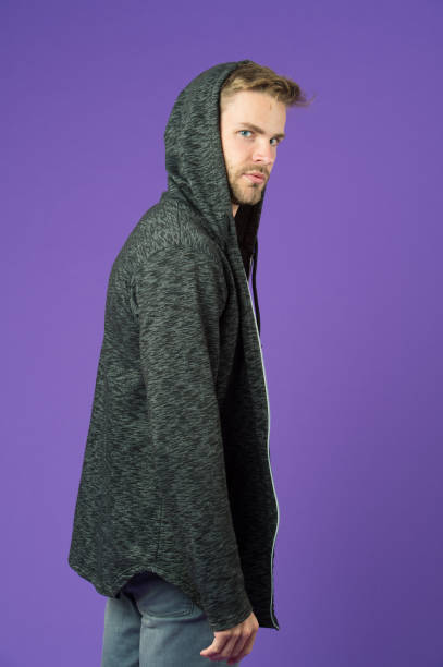 l’homme barbu porte le capuchon sur le fond violet. homme dans le sweat-shirt occasionnel. modèle de mode dans le sweat à capuche gris. mode de vie actif et activité de santé. mode sport ou style et concept de tendance - hooded shirt men macho hood photos et images de collection