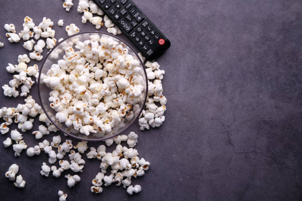 Top view of a bowl of popcorn and tv remote on black background Top view of a bowl of popcorn and tv remote on table . remote control on table stock pictures, royalty-free photos & images