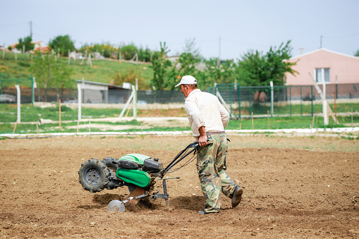 Man working with plow machine in the garden in spring field