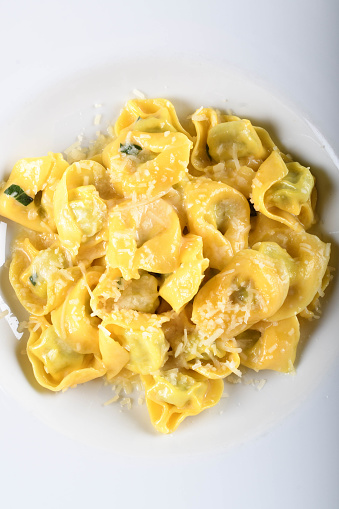 Tortellini with ricotta cheese and spinach, butter, sage sauce, grated parmesan. Parmigiano-Reggiano flakes over traditional italian pasta cooked, served in white plate, over brown table in restaurant