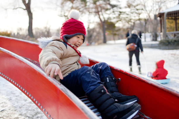 Happy boy on a slide outdoors. A eight years old boy playing in the public park on a cold winter day. children in winter stock pictures, royalty-free photos & images