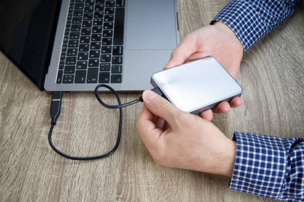 Office worker disconnects portable hard disk drive from a computer Male hands in blue checked shirt disconnect an external hard drive from the laptop. external hard disk drive stock pictures, royalty-free photos & images