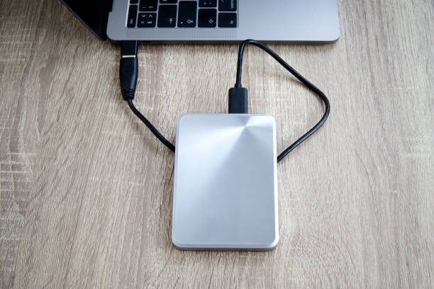 Portable hard drive connected to a laptop computer on a woo den table.