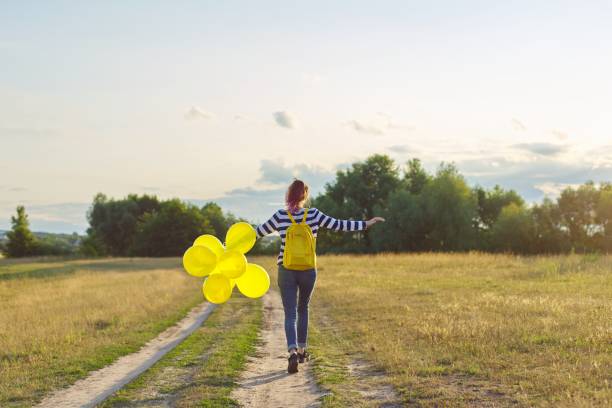 szczęśliwa nastolatka z balonami biega i skacze wzdłuż wiejskiej drogi - teenagers only lake summer sunlight zdjęcia i obrazy z banku zdjęć