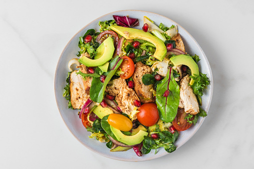 Salad with grilled chicken breast, avocado, pomegranate seeds and tomato on white background. healthy diet food. Top view
