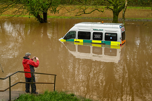 Nantgarw, Near Cardiff, Wales - February 2020: Person taking a picture of an ambulance submerged in storm water after the River Taff burst its banks near Cardiff.