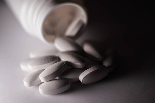 белая добавка таблетки разлив из бутылки - drug abuse narcotic medicine protection стоковые фото и изображения