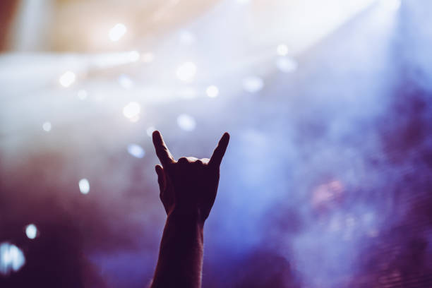 Horns raised up by a metalhead in the crowd in front of stage during the band's performance Horns raised up by a metalhead in the crowd in front of stage during the band's performance rock group photos stock pictures, royalty-free photos & images