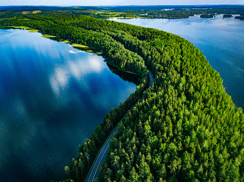 Aerial view of road with cars between green forest and blue lake water in summer Finland