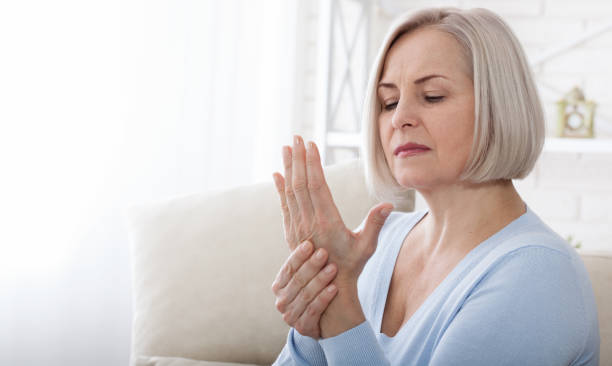 mujer masajeando su mano y muñeca artrítica - arthritis fotografías e imágenes de stock