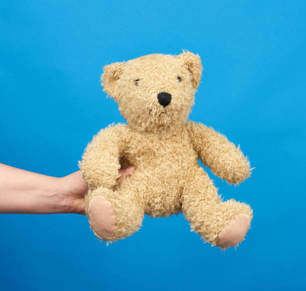 istock female hand hold a small brown toy teddy bear on a blue background, 1226753711