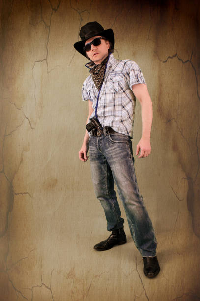 istock Cool armed young man in jeans and in sunglasses standing with a gun and looking forward menacing. 1226756131