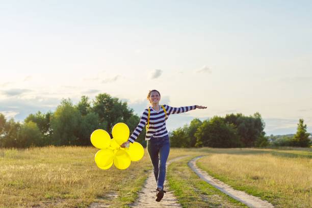 glückliches teenager-mädchen mit luftballons laufen und springen entlang landstraße - arms outstretched teenage girls jumping flying stock-fotos und bilder