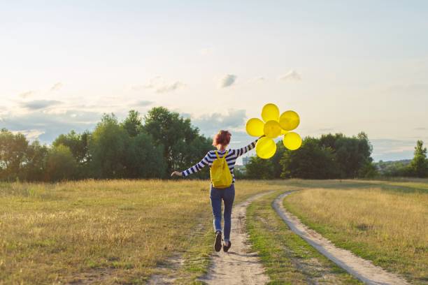 glückliches teenager-mädchen mit luftballons laufen und springen entlang landstraße - arms outstretched teenage girls jumping flying stock-fotos und bilder