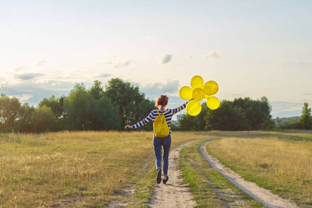 happy teenager girl with balloons running and jumping along country road - arms outstretched teenage girls jumping flying imagens e fotografias de stock