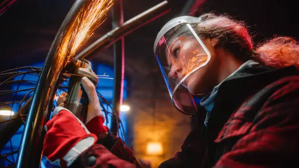 Close Up of a Talented Innovative Tomboy Female Artist Using an Angle Grinder to Make Abstract, Brutal and Expressive Metal Sculpture in a Workshop. Contemporary Fabricator Creating Modern Steel Art.