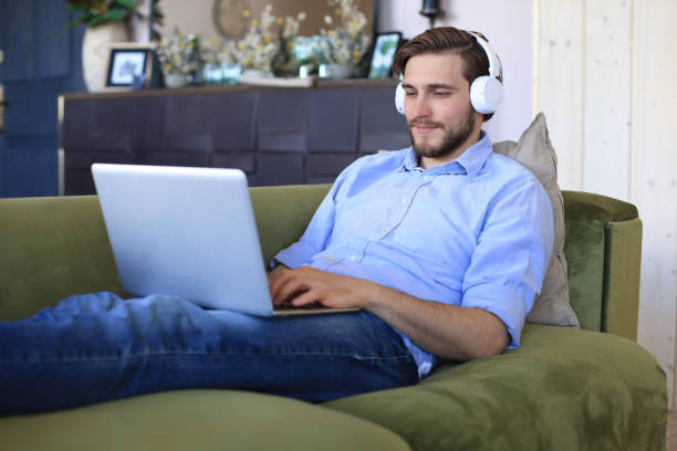 istock Concentrated young freelancer businessman sitting on sofa with laptop, working remotely online at home. 1226764678