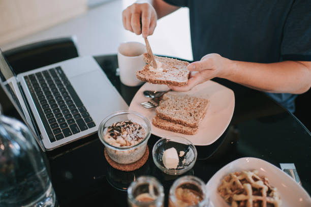 un adulto medio cinese asiatico che fa colazione in sala da pranzo mentre utilizza laptop per rispondere alle e-mail al mattino - non alcoholic beverage comfort food snack dining table foto e immagini stock