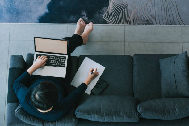 um adulto asiático médio chinês tomando café da manhã na sala de jantar enquanto usa laptop para responder e-mails na parte da manhã - um dia na vida de - fotografias e filmes do acervo