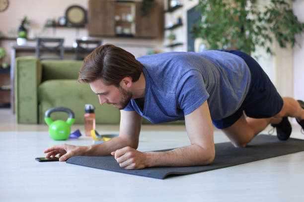 istock Attractive beared man looking into smartphone and doing plank exercise at home during quarantine. Fitness is the key to health. 1226764987