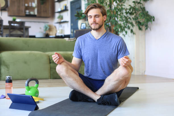 istock Young handsome man is practicing yoga in lotus pose sitting on the floor at home during quarantine. Sport is foundation of healthy life. 1226765548