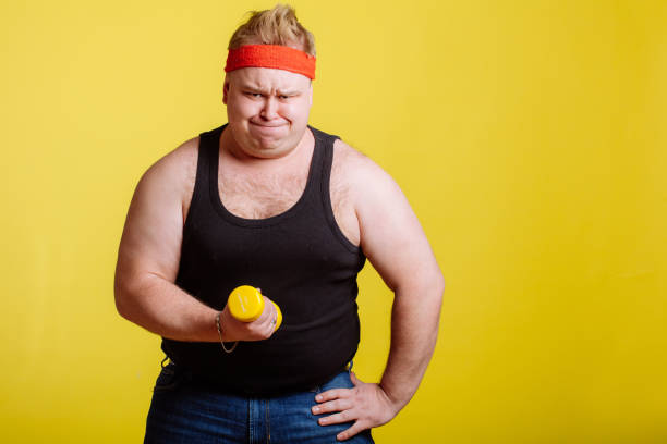 istock Fat man try to lift small yellow dambbell 1226769252