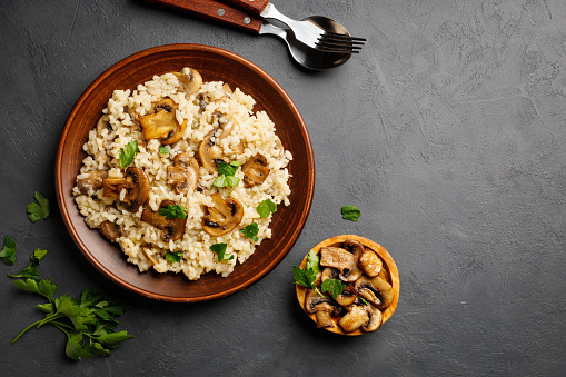 A dish of Italian cuisine - risotto from rice and mushrooms in a brown plate on a black slate background. Above view. Copy space for text.