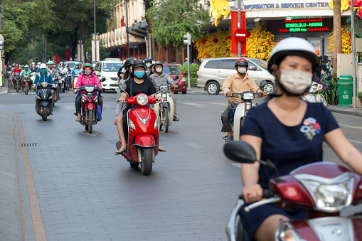 Ho Chi Minh, Vietnam - March, 1, 2020: Many Vietnamese people riding motorbikes motorcycles on road wearing masks